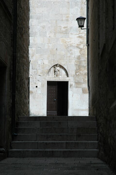The gothic portal of the Church of Saint Nicholas in Korcula features a stone relief of Jesus the Good Shepherd in the pointed tympanum above a wooden door