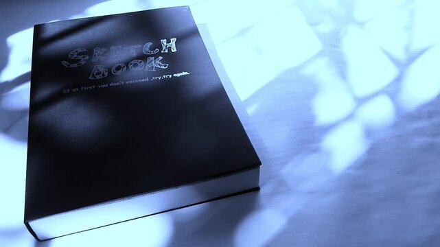 Black Sketchbook With Motivational Quote Under Soft Blue Light And Abstract Shadows