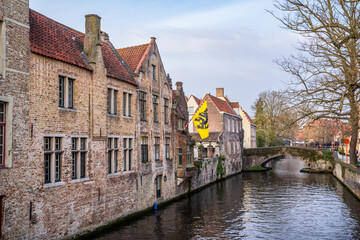 Obraz premium Historic brick houses and canal in Bruges with Flanders flag.
