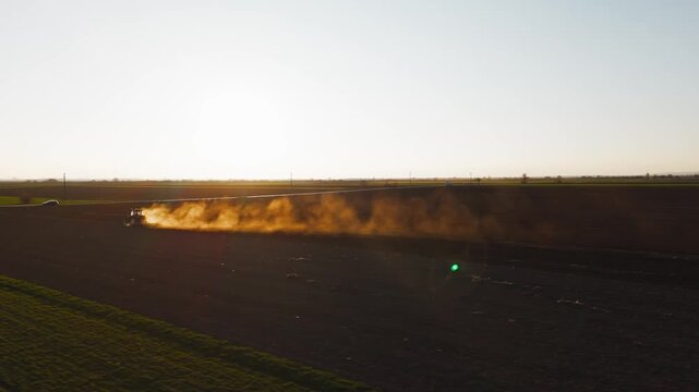 Aerial view of a tractor at work, tilling the dark brown soil, creating a plume of dust under the bright sky, Jazak, Vojvodina, Serbia.