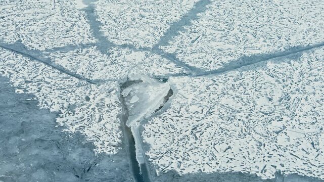 Frozen lake shows cracks and frost covering the surface. The ice forms a unique pattern under bright sunlight. This scene captures the beauty of winter weather in a natural setting.