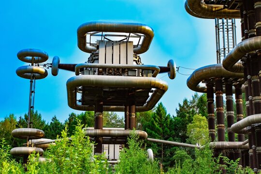 High voltage Tesla tower lightning generator in green forest landscape under blue sky background.