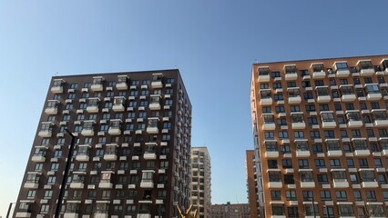Fototapeta premium Modern multi-story residential buildings with distinct brown and orange facades and white balconies against a clear blue sky.