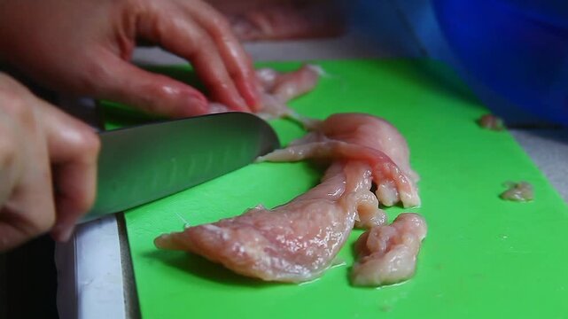 Fresh raw chicken breast fillet being cut with a knife