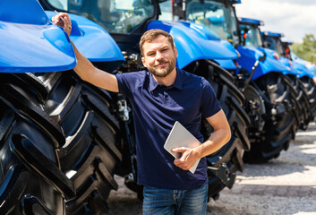 Modern male farmer holding tablet near tractors at farm equipment dealership.  © Igor Barilo