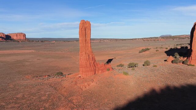 A cinematic drone rotation circles an epic red rock spire monolith, emphasizing the mystical verticality and rugged sandstone beauty of a legendary landmark within a remote desert vista.