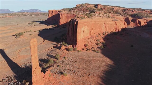 This drone shot features a lone red rock spire monolith framed by a deep desert canyon, showcasing the dramatic geological verticality and mysterious beauty of a remote arid wilderness landscape.