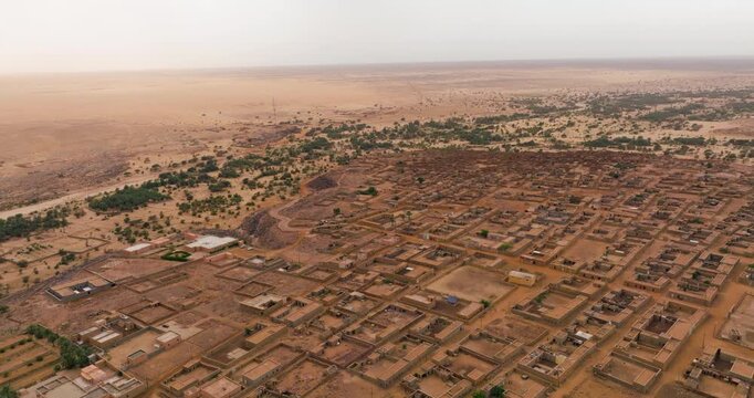 Ancient Desert Town of Ouadane In Mauritania, With Earth-toned Buildings And Nearby Oasis Of Green Trees. aerial orbiting shot