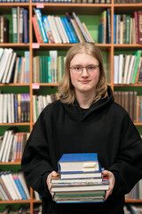 Young smiling man in a library holding stack of books