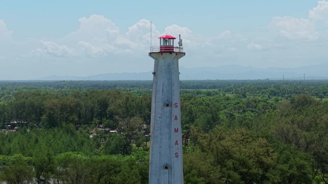 Aerial view of Mercusuar Samas lighthouse standing tall against the backdrop of lush greenery and the calming blue sea, Bantul Regency, Daerah Istimewa Yogyakarta, Indonesia.