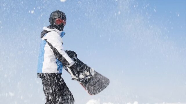 Snowboarder in full gear with helmet and ski goggles scooping snow and throwing it up. Fun and drive at ski resort. Happiness from active lifestyle. Winter and sport