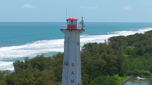 Aerial view of Mercusuar Samas lighthouse with the backdrop of the ocean's turquoise waters meeting the sandy shore, Bantul Regency, Daerah Istimewa Yogyakarta, Indonesia.