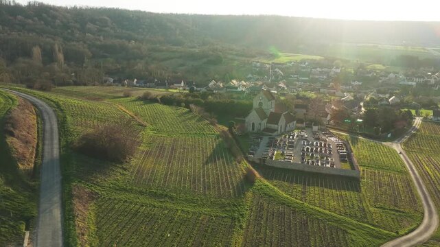 Aerial view of church and graveyard surrounded by fields, bathed in warm sunlight, contrasting with the shadows, Courthiezy, Grand Est, France.