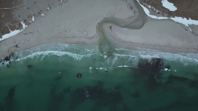 Aerial view of the shore where Uttakleivveien meets the sea, a study in contrasts with the white waves meeting the dark sea, Hauklandstranda, Nordland, Norway.