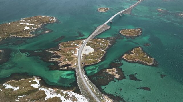 Aerial view of the Flakstadbruene bridge cutting across the turquoise waters, connecting islands with patches of snow, Flakstadbruene, Nordland, Norway.