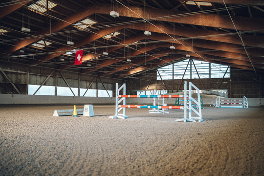 Empty indoor arena setup for show jumping with colorful obstacles and a swiss flag overhead