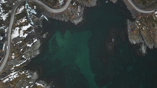 Aerial view of a winding road snaking along the rugged coastline, juxtaposing the dark, rocky terrain with the turquoise waters, Tind, Nordland, Norway.