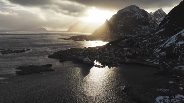 Aerial view of the village of Tind nestled between rugged mountains, the sun casts golden rays over the dark waters, creating a stunning contrast, Tind, Nordland, Norway.