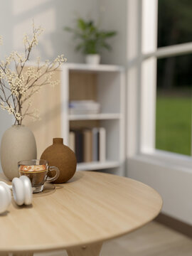 Coffee cup and flower vases on round wooden table across bookshelf and window in modern room or cafe