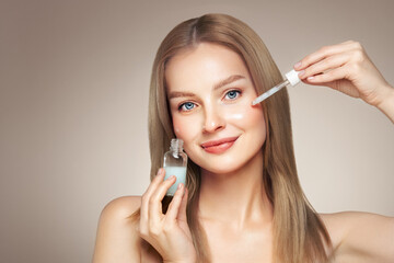 Young beautiful blonde woman applying face serum with pipette. Cosmetic procedures for facial skin care