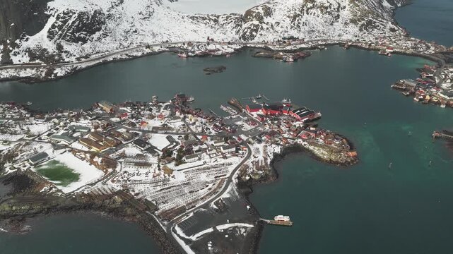 Aerial view of Reinebringen in winter, a picturesque scene with snow-dusted buildings and mountains meeting the frigid waters, Reine, Nordland, Norway.
