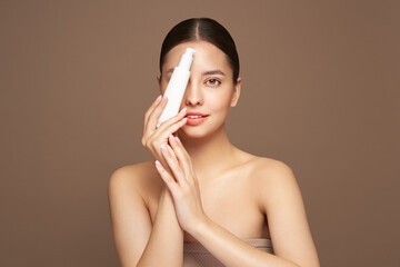 Beautiful woman with bottle of moisturizer cream. Video of woman with perfect skin on beige background. Beauty and Skin care concept