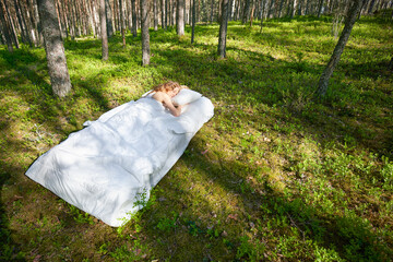 Woman sleeps on a mattress in the summer forest. The girl is resting in nature