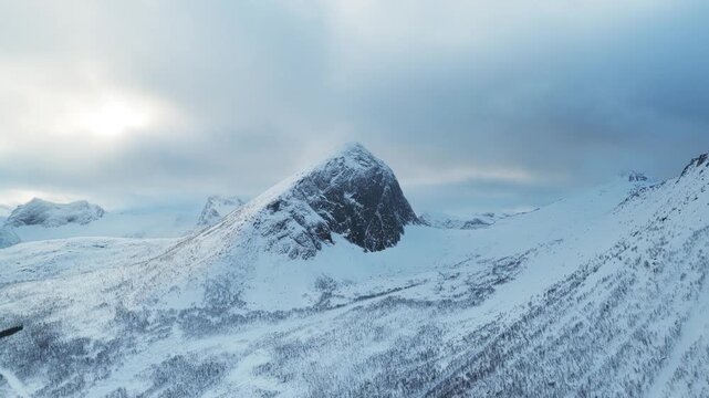 Aerial view of the snow-capped Segla mountain peak under a cloudy sky, a stark contrast of white and grey in the landscape, Fjordgard, Troms, Norway.