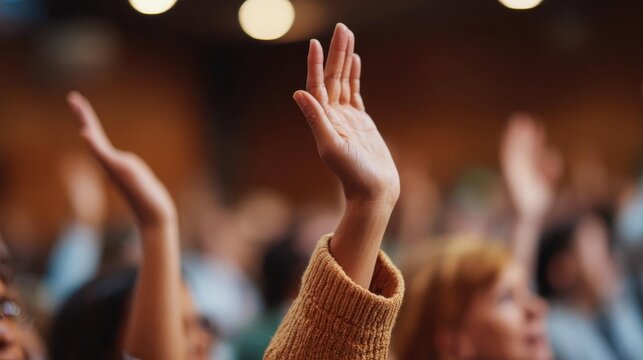 Close-up of a person's hands raised up in the air, with their fingers spread wide. the person is wearing a brown sweater and appears to be standing in front of a crowd of people.