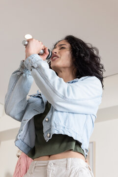 Female singer in her 20s singing, holding microphone and wearing denim jacket crop top in rehearsal