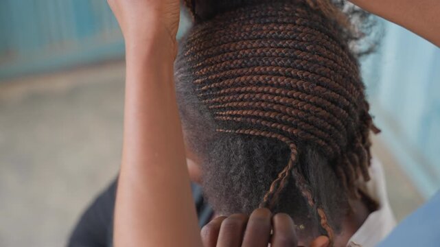 Finished cornrows showcase neat scalp rows, hands adjusting edges and securing ends, sleek protective styling for daily wear, confident client posture, outdoor market salon vibe, skilled stylist final