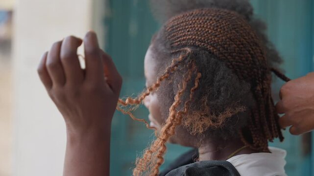 Closeup braids being loosened to reveal curly ends and powdery residue, stylist detangling extensions with gentle grip, outdoor doorway backdrop, candid profile, transformation from tight rows to free