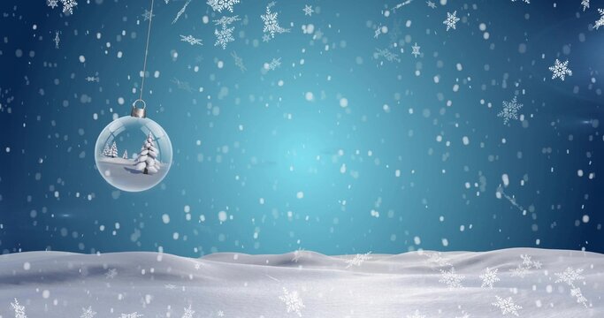 Hanging glass bauble showing mini pine trees over snowy field, with falling snowflakes, copy space