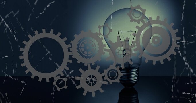 Glowing clear incandescent bulb with filament casting halo on dark tabletop, gears overlay