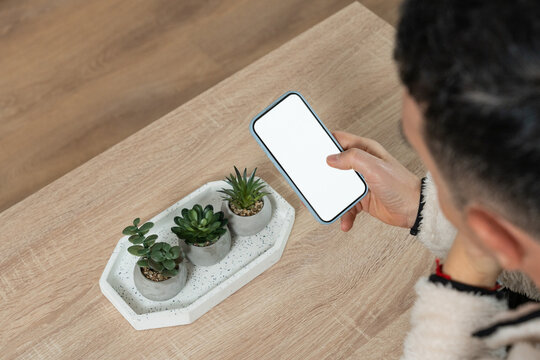 Hand holding smartphone with blank screen over wooden table