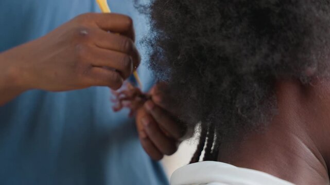 Closeup hands braiding black hair in gentle home setting, stylist sections nape with comb and fingers, creating tight twists and textured rows warm soft light, tactile care, patient technique,
