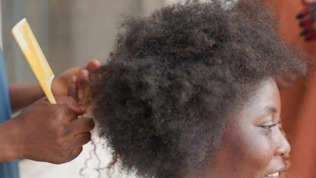 Sideprofile woman with afro hair stylist gently detangles and separates coils using comb and fingers revealing texture and movement warm indoor setting patient technique transforming tangled sections
