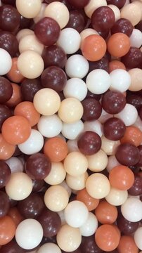 Vertical close up video of plastic ball pit balls in brown cream and orange colors forming playful textured background