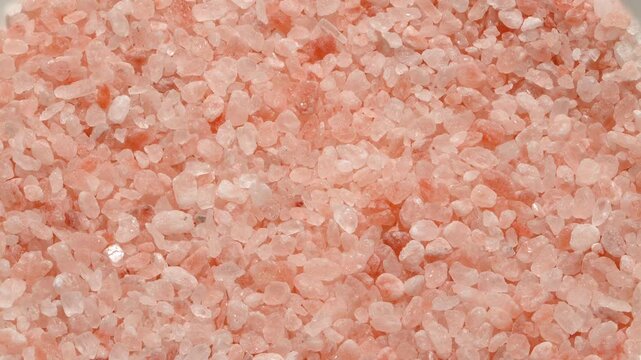 Macro rotating background of coarse pink Himalayan salt crystals from Pakistan. Pure organic mineral texture for culinary, spa and wellness projects.