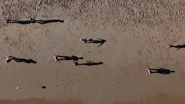 Aerial view of people playing on the light brown sandy beach casting long shadows, their figures scattered across the expansive shore, Cascais, Lisbon, Portugal.
