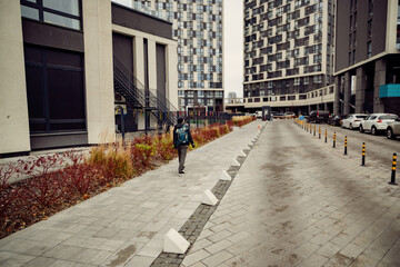 Man with Backpack Walking Through a Modern Residential Complex Courtyard with High-Rise Buildings © dizfoto1973
