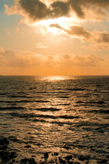 Fototapeta premium Dramatic orange sunset clouds over dark ocean waves with sun rays