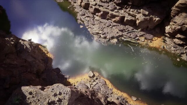 Abstract canyon reflection from above, calm jade water winding between textured rock formations, soft cloud mirrors and glittering highlights produce painterly