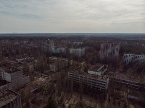 Aerial view of abandoned apartment blocks surrounded by overgrown forest under a cloudy sky in Pripyat, Kyiv Oblast, Ukraine.