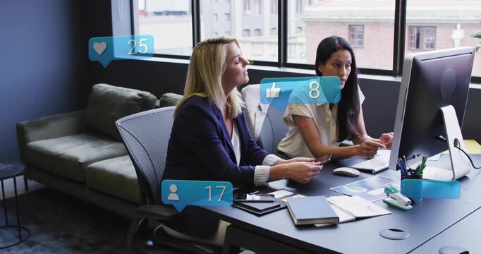 Two coworkers tapping phone, clicking monitor, causing floating likes while reviewing marketing