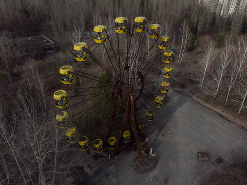Aerial view of the abandoned Ferris wheel with yellow cabins and rusty metal structure surrounded by bare trees in Pripyat, Kyiv Oblast, Ukraine.