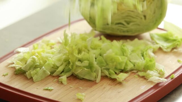 Chopping fresh iceberg lettuce on wooden cutting board, close up of healthy salad preparation on light background