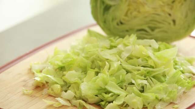 Chopping fresh iceberg lettuce on wooden cutting board, close up of healthy salad preparation on light background