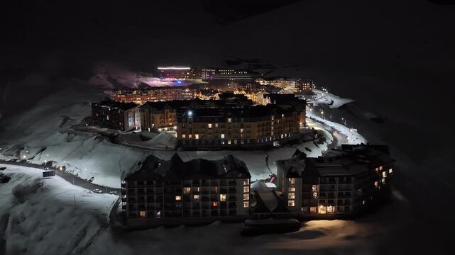 Night Drone view of Gudauri in Georgia town with snow covered mountains, ski slopes and town after fresh snowfall in winter season. Gudauri ski resort with fresh powder snow, Georgia.