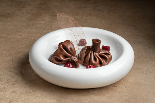 Creative chocolate dessert shaped like khinkali with berries and decoration served on white plate